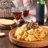 Polenta con funghi, perfetta con un buon vino da abbinare alla polenta. Due calici rossi e una bottiglia completano la scena rustica.