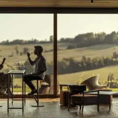 Coppia degusta vino in un'elegante sala con vista sulle colline. Un'esperienza di cantine con pernottamento in Piemonte.