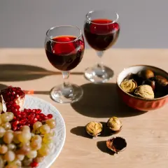 Due calici di vino rosso, uva, melograno e castagne, un'ambientazione che evoca un senso di abboccato significato, quasi un invito a gustare i piaceri semplici.