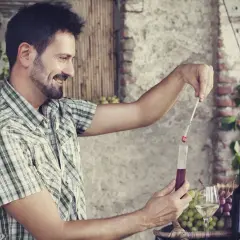 Un uomo controlla l'acidità volatile del vino con un densimetro, circondato da uva e bottiglie.