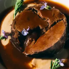 Arrosto succulento in salsa scura, guarnito con rosmarino e fiori viola. Perfetto per i barbera d'asti abbinamenti.