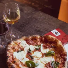 Una pizza fumante con mozzarella e basilico, accompagnata da calici di vino rosso e bianco, perfetti per un'ottima pizza.