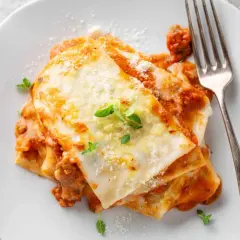 Porzione di lasagne al ragù, ricca e fumante, con besciamella e parmigiano. Perfetta con un buon vino per lasagne.