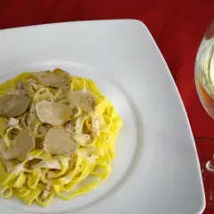 Tagliatelle con crema e scaglie di tartufo bianco, accanto un calice di vino da abbinare al tartufo bianco.