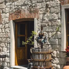 Ingresso di "Cinque Quinti", un negozio con insegna in ferro battuto, un torchio antico e vasi di fiori rossi.