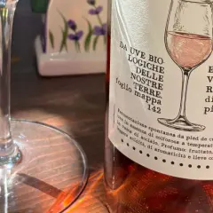 Calice vuoto e bottiglia di vino rosato, pronti per una degustazione vini Sicilia. L'etichetta descrive uve biologiche e note fruttate.
