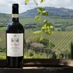 Bottiglia di Vino Nobile di Montepulciano Riserva su un barile, con vigneti e colline toscane sullo sfondo. Ideale per una degustazione vini Montepulciano.