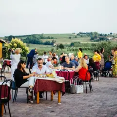 Un conviviale pranzo in vigna Monferrato, con tavoli apparecchiati all'aperto e persone che chiacchierano e gustano il cibo, sullo sfondo dolci colline.