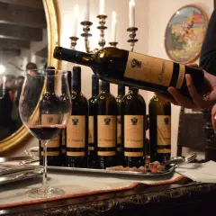 Degustazione di vini delle cantine Goretti: una bottiglia viene versata in un calice, con altre bottiglie e bicchieri su un vassoio.