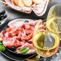 Tagliere di salumi e formaggi con olive, pane e due calici di vino frizzante. Perfetti moscato d'asti abbinamenti per un aperitivo.