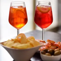 Due cocktail colorati, patatine, olive e pizzette per un romantico aperitivo serale.