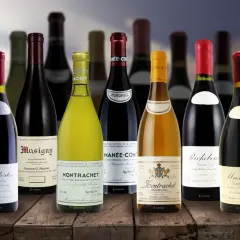 Una selezione di bottiglie costose di vino pregiato, tra cui Montrachet e Musigny, disposte su un tavolo di legno.