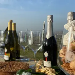 Bottiglie di vino dolce Asti, bicchieri, torta e dolcetti in un allestimento all'aperto.