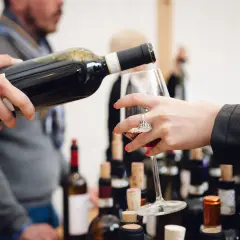 Un bicchiere viene riempito durante una degustazione di Barolo nelle Langhe, tra bottiglie e tappi di sughero.