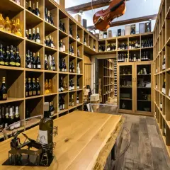 Cantine siciliane con scaffalature in legno piene di bottiglie di vino, un violino appeso e un tavolo in legno massiccio.