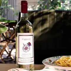 Bottiglia di vino bianco Vermentino Valcolomba, ideale vino per frittura di pesce, accanto a un piatto di spaghetti.