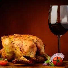 Pollo arrosto dorato con contorno di verdure fresche e un bicchiere di vino rosso, perfetto vino da abbinare al pollo.