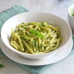 Piatto di trofie al pesto, con mortaio e basilico. Un'idea su cosa abbinare alla pasta al pesto per un pasto fresco e gustoso.