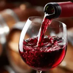 Versando vino rosso in un calice, con botti di legno sullo sfondo. Un sorso di il dolcetto.