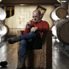 Uomo assapora vino Franz Haas in cantina tra botti.