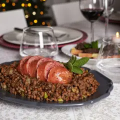 Piatto di cotechino affettato su lenticchie, pronto per essere gustato con un buon vino da abbinare al cotechino.