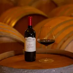 Bottiglia e calice di vino rosso su una botte, con botti di legno sullo sfondo. Un assaggio del governo toscano vino.