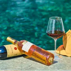 Due bottiglie di vino e un bicchiere pieno, con uno sfondo acquatico turchese. Un'immagine che evoca il sapido significato del relax e del piacere.