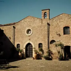 L'abbazia Santa Anastasia, con la sua facciata in pietra e il campanile, si affaccia su un cortile acciottolato.