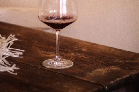 Un calice di vino rosso riposa su un tavolo di legno rustico, pronto per una degustazione vini Langhe.