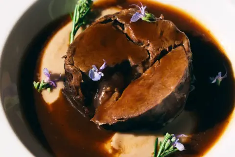 Arrosto succulento in salsa scura, guarnito con rosmarino e fiori viola. Perfetto per i barbera d'asti abbinamenti.