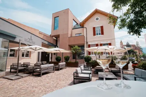 Terrazza accogliente con divani e ombrelloni, due calici di vino bianco in primo piano. La cantina St. Pauls sullo sfondo.