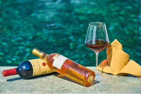 Due bottiglie di vino e un bicchiere pieno, con uno sfondo acquatico turchese. Un'immagine che evoca il sapido significato del relax e del piacere.