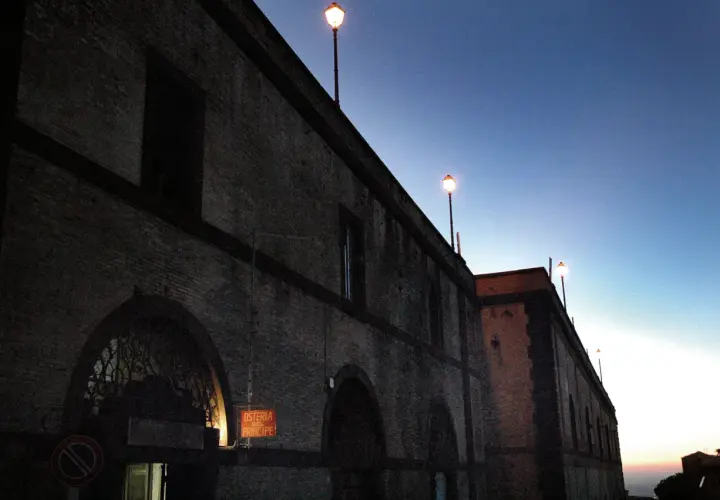 Edificio in mattoni con lampioni accesi al crepuscolo. L'insegna "Osteria del Principe" evoca il **frasca significato** di un luogo conviviale.