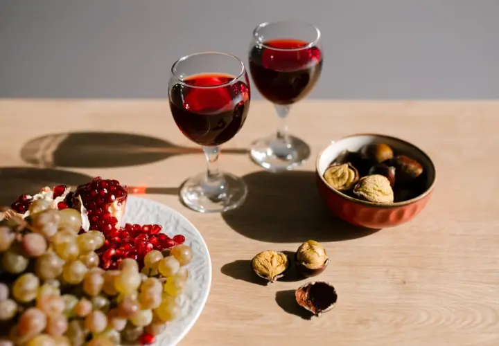 Due calici di vino rosso, uva, melograno e castagne, un'ambientazione che evoca un senso di abboccato significato, quasi un invito a gustare i piaceri semplici.