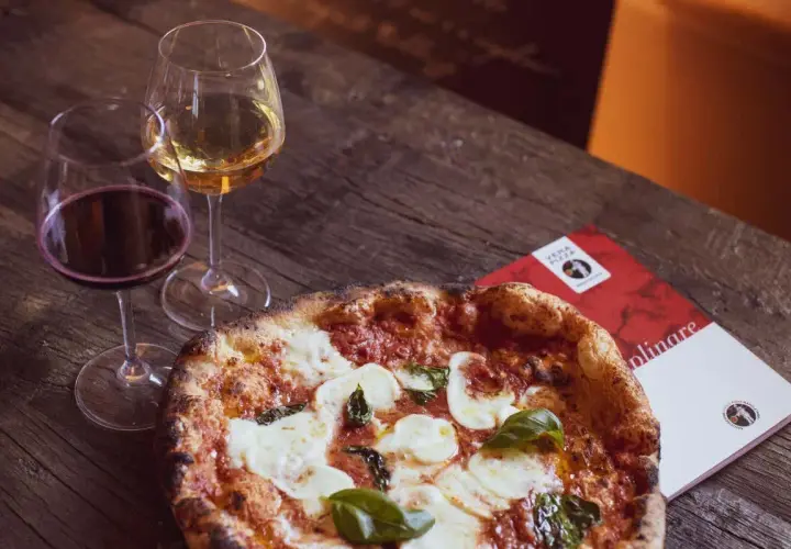 Una pizza fumante con mozzarella e basilico, accompagnata da calici di vino rosso e bianco, perfetti per un'ottima pizza.