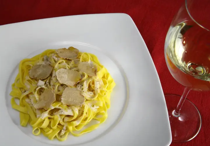 Tagliatelle con crema e scaglie di tartufo bianco, accanto un calice di vino da abbinare al tartufo bianco.