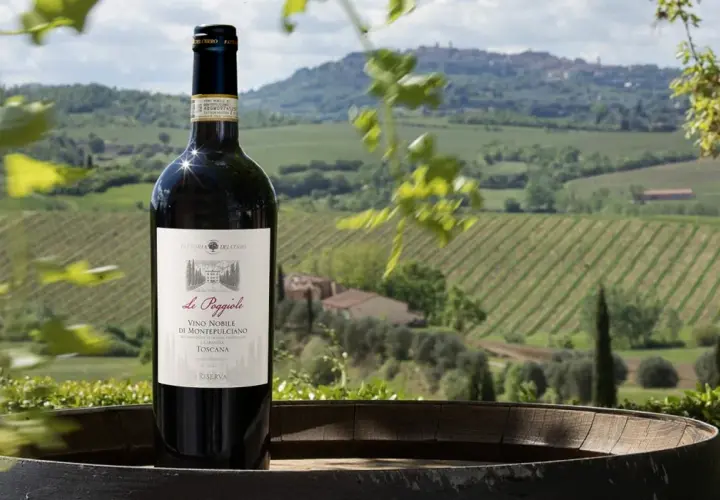 Bottiglia di Vino Nobile di Montepulciano Riserva su un barile, con vigneti e colline toscane sullo sfondo. Ideale per una degustazione vini Montepulciano.