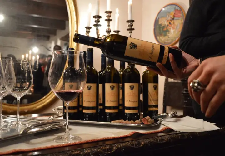 Degustazione di vini delle cantine Goretti: una bottiglia viene versata in un calice, con altre bottiglie e bicchieri su un vassoio.