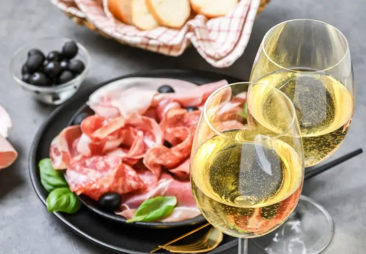 Tagliere di salumi e formaggi con olive, pane e due calici di vino frizzante. Perfetti moscato d'asti abbinamenti per un aperitivo.