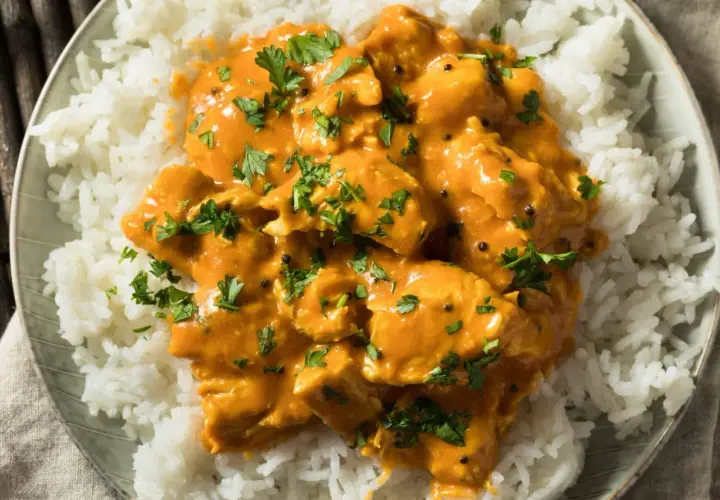 Pollo al curry cremoso su riso bianco, guarnito con prezzemolo fresco. Un vino da abbinare al pollo al curry? Un Gewürztraminer o un Riesling.