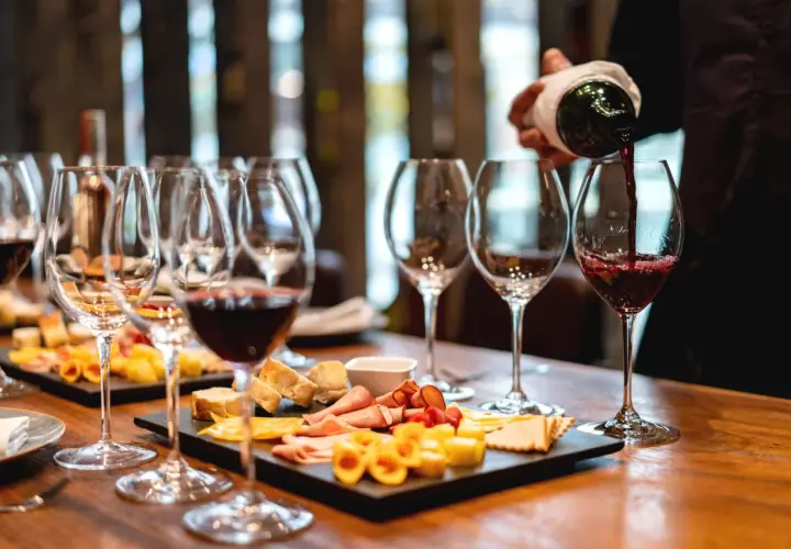 Calice di vino rosso versato, con taglieri di formaggi e salumi. Perfetti abbinamenti per un vino vespaiolo.