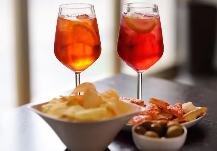 Due cocktail colorati, patatine, olive e pizzette per un romantico aperitivo serale.