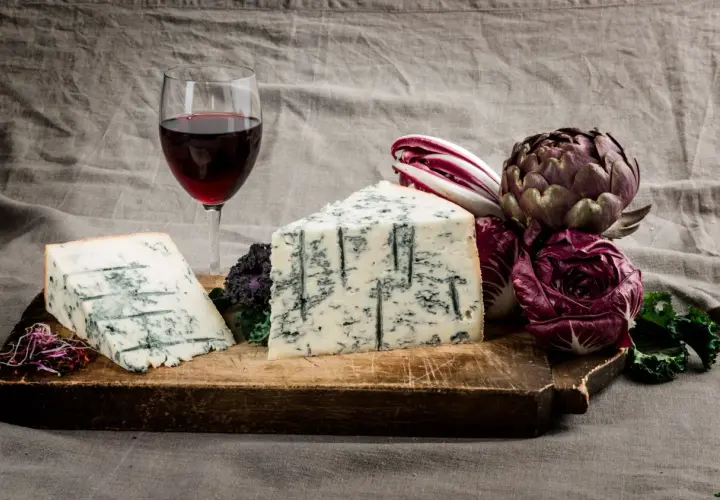 Gorgonzola e vino rosso su tagliere rustico, con radicchio e carciofo. Un perfetto gorgonzola abbinamento vino per un'esperienza gustativa.