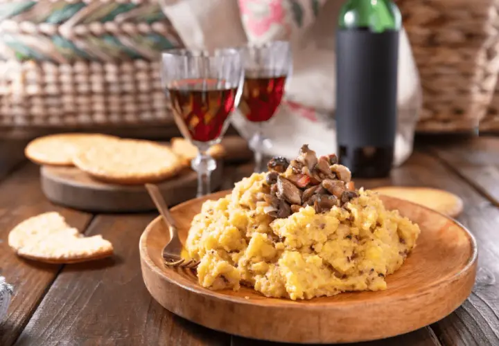 Polenta con funghi, perfetta con un buon vino da abbinare alla polenta. Due calici rossi e una bottiglia completano la scena rustica.
