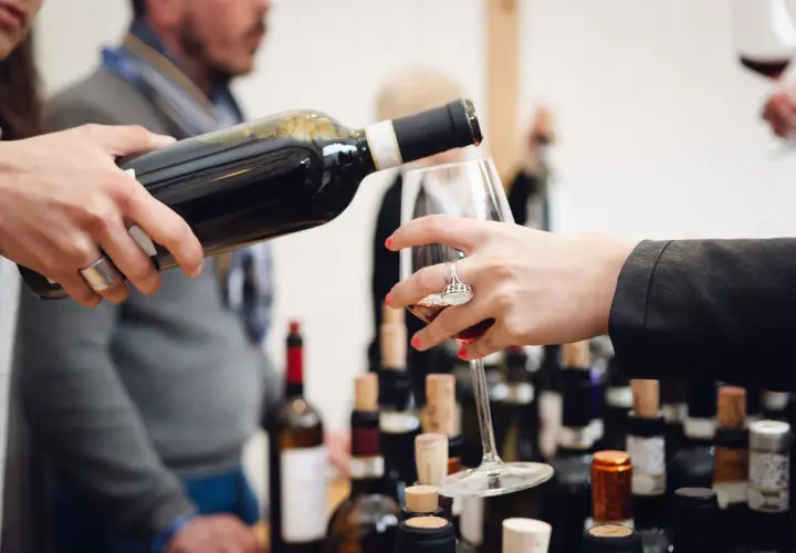 Un bicchiere viene riempito durante una degustazione di Barolo nelle Langhe, tra bottiglie e tappi di sughero.