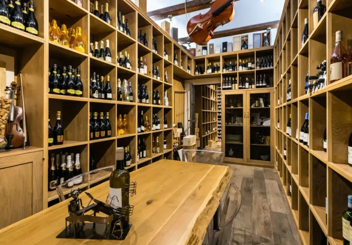 Cantine siciliane con scaffalature in legno piene di bottiglie di vino, un violino appeso e un tavolo in legno massiccio.