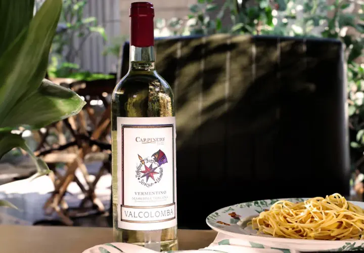 Bottiglia di vino bianco Vermentino Valcolomba, ideale vino per frittura di pesce, accanto a un piatto di spaghetti.