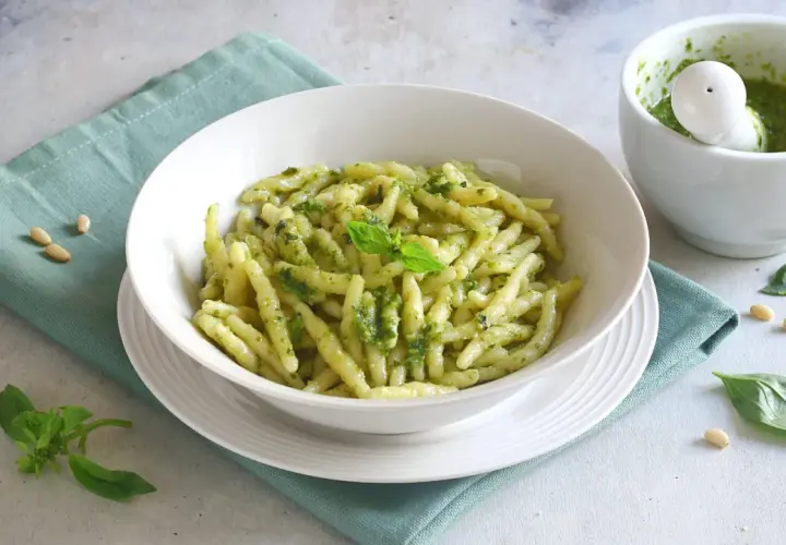 Piatto di trofie al pesto, con mortaio e basilico. Un'idea su cosa abbinare alla pasta al pesto per un pasto fresco e gustoso.