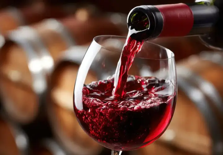 Versando vino rosso in un calice, con botti di legno sullo sfondo. Un sorso di il dolcetto.