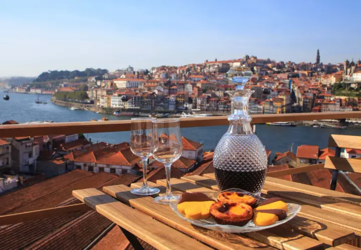 Un bicchiere di late bottled vintage porto, due calici e dolcetti su un tavolo con vista sulla città di Porto.